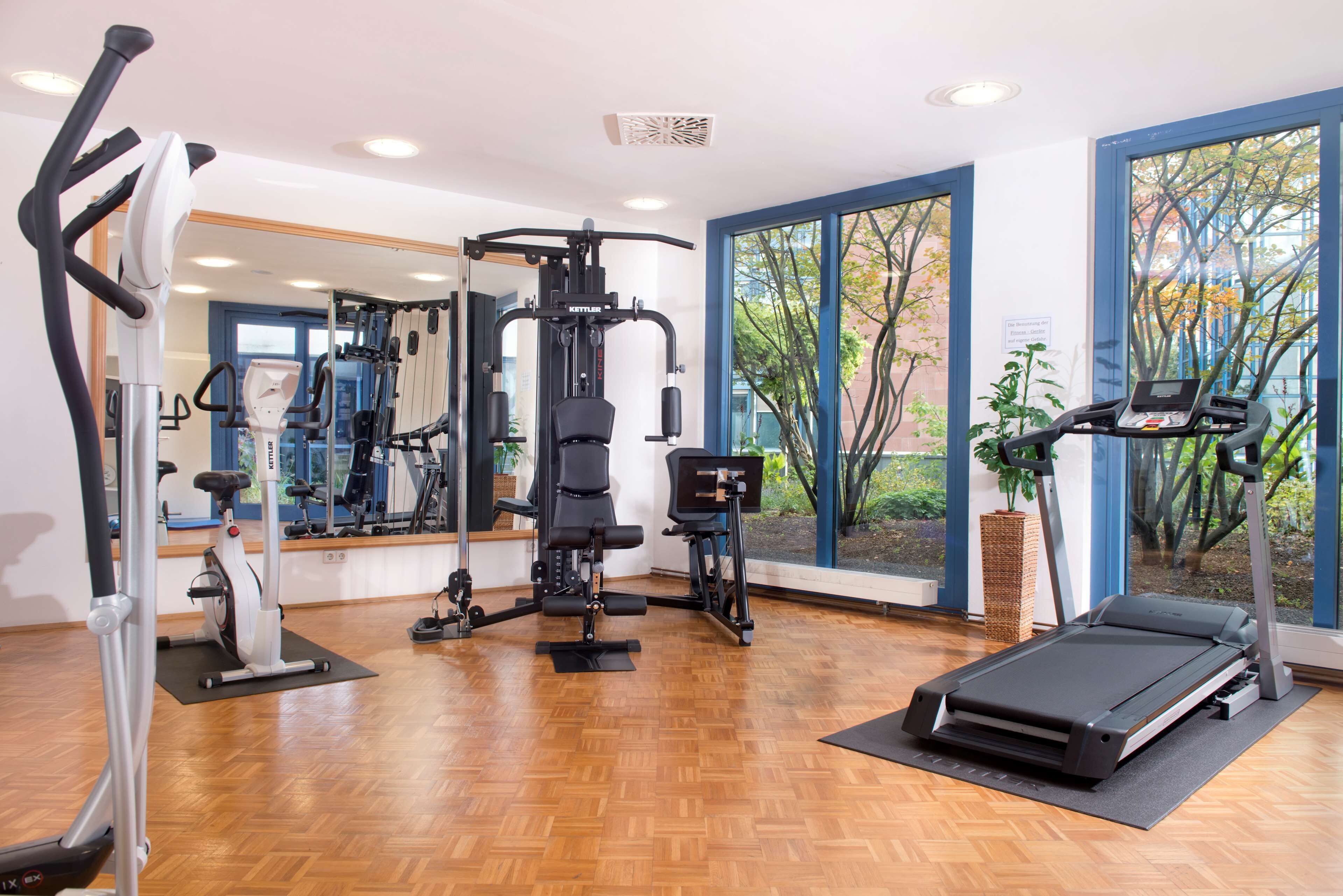 Ein Fitnessstudio mit Trainingsgeräten, großen Fenstern und Holzboden.