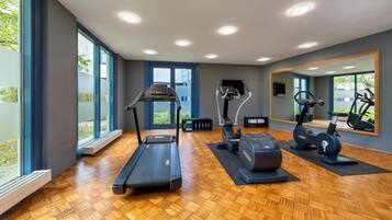 Ein modernes Fitnessstudio mit Laufband, Crosstrainer und Ergometer, großen Fenstern und Spiegeln.
