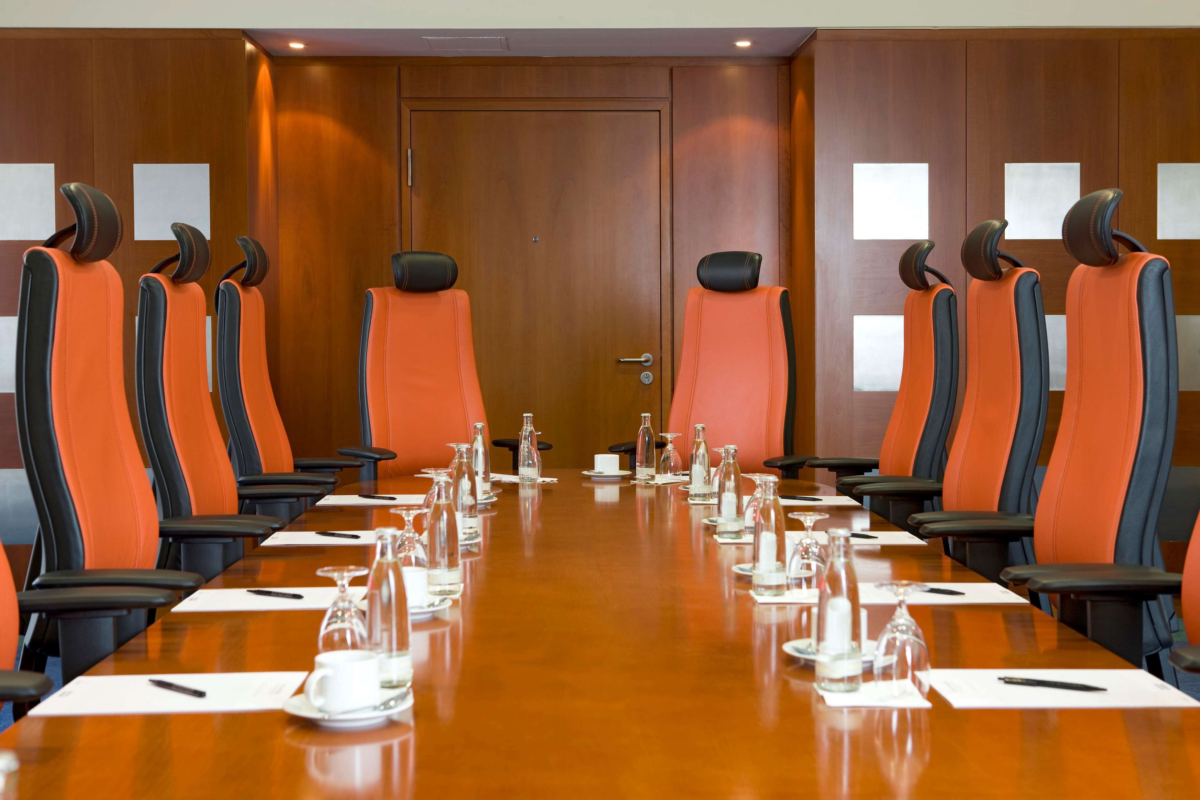 Une salle de conférence avec une longue table, de nombreuses chaises et des bouteilles d’eau.