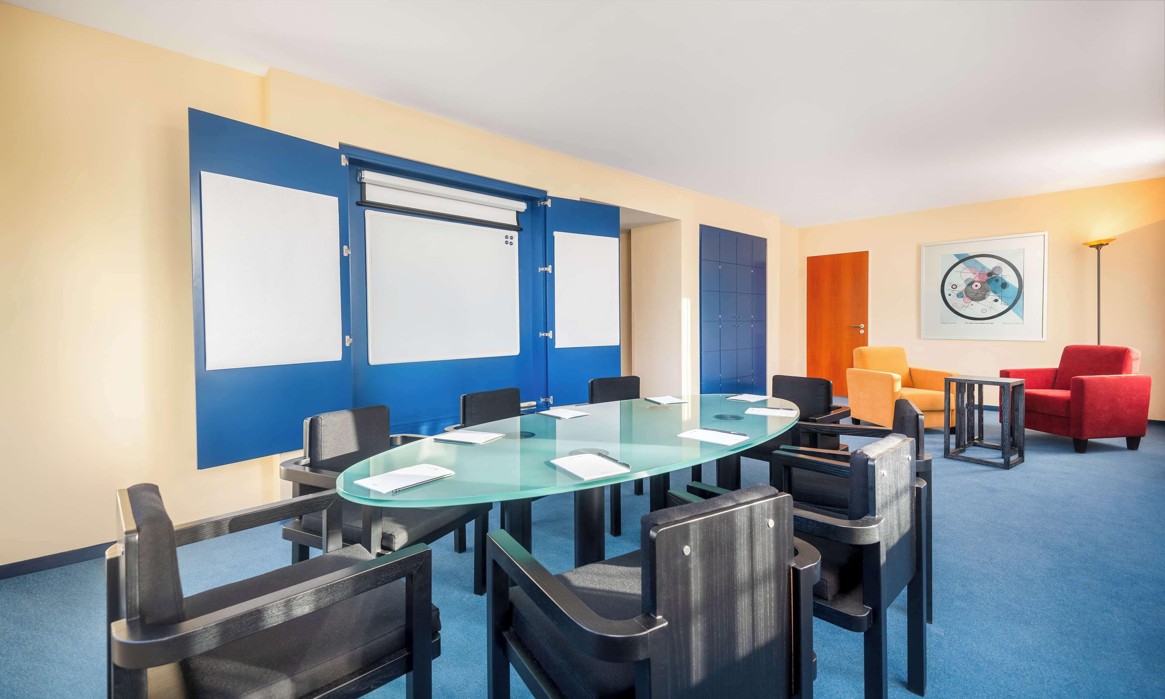 A conference room with a glass table, black chairs, a red armchair, and a blue door.