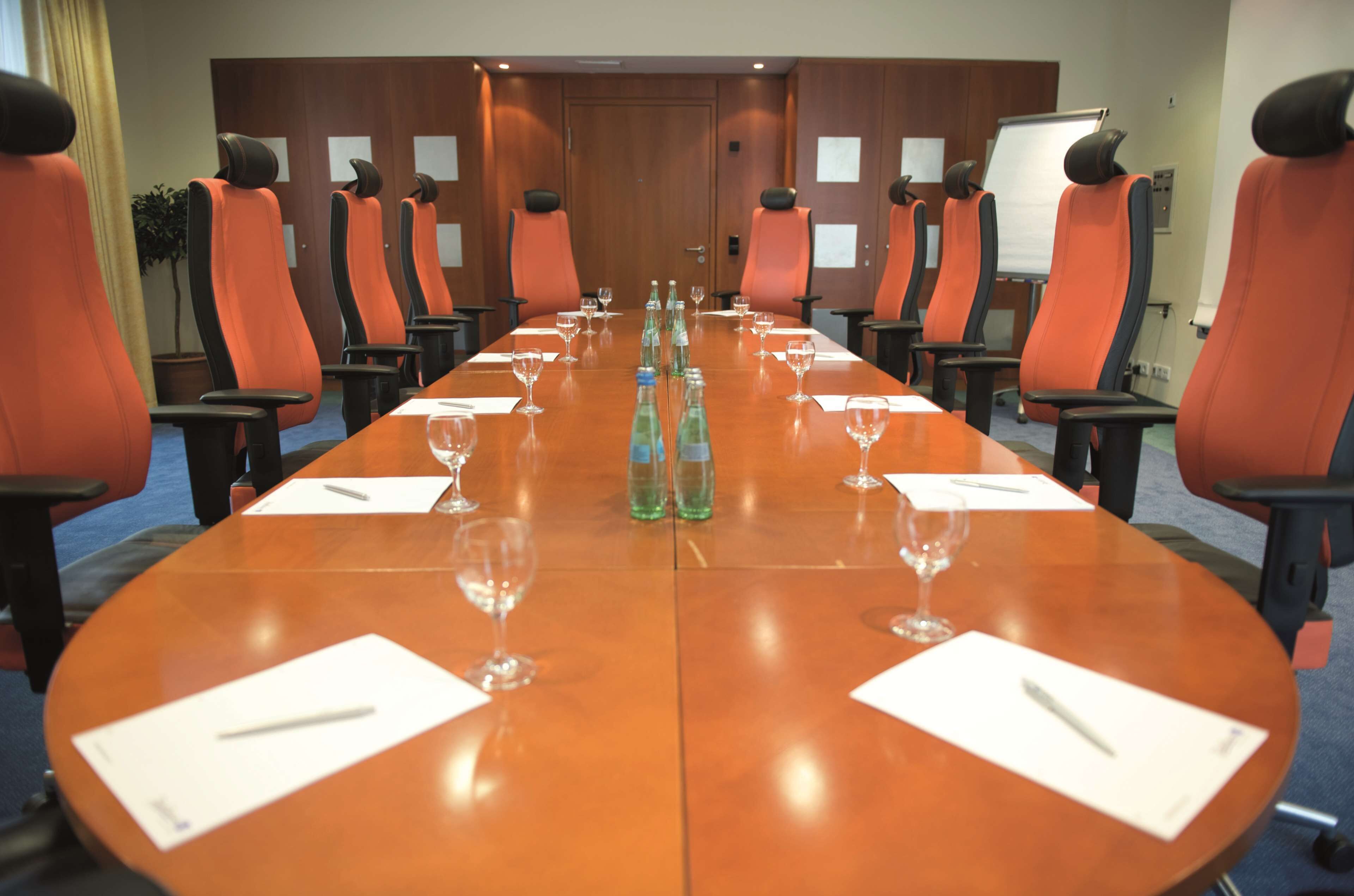 Ein Konferenzraum mit langem Tisch, orangefarbenen Stühlen, Wasserflaschen und Gläsern.
