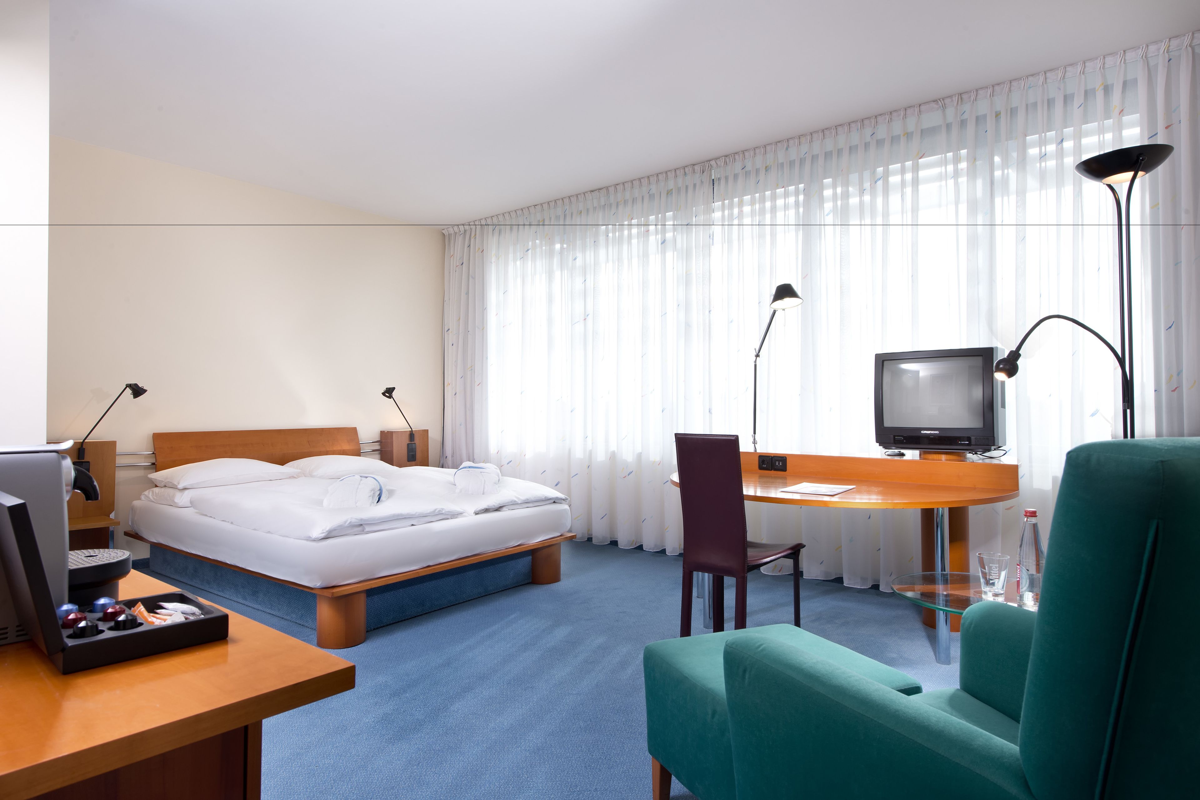A hotel room with a bed, desk, chair, television, and a desk lamp.