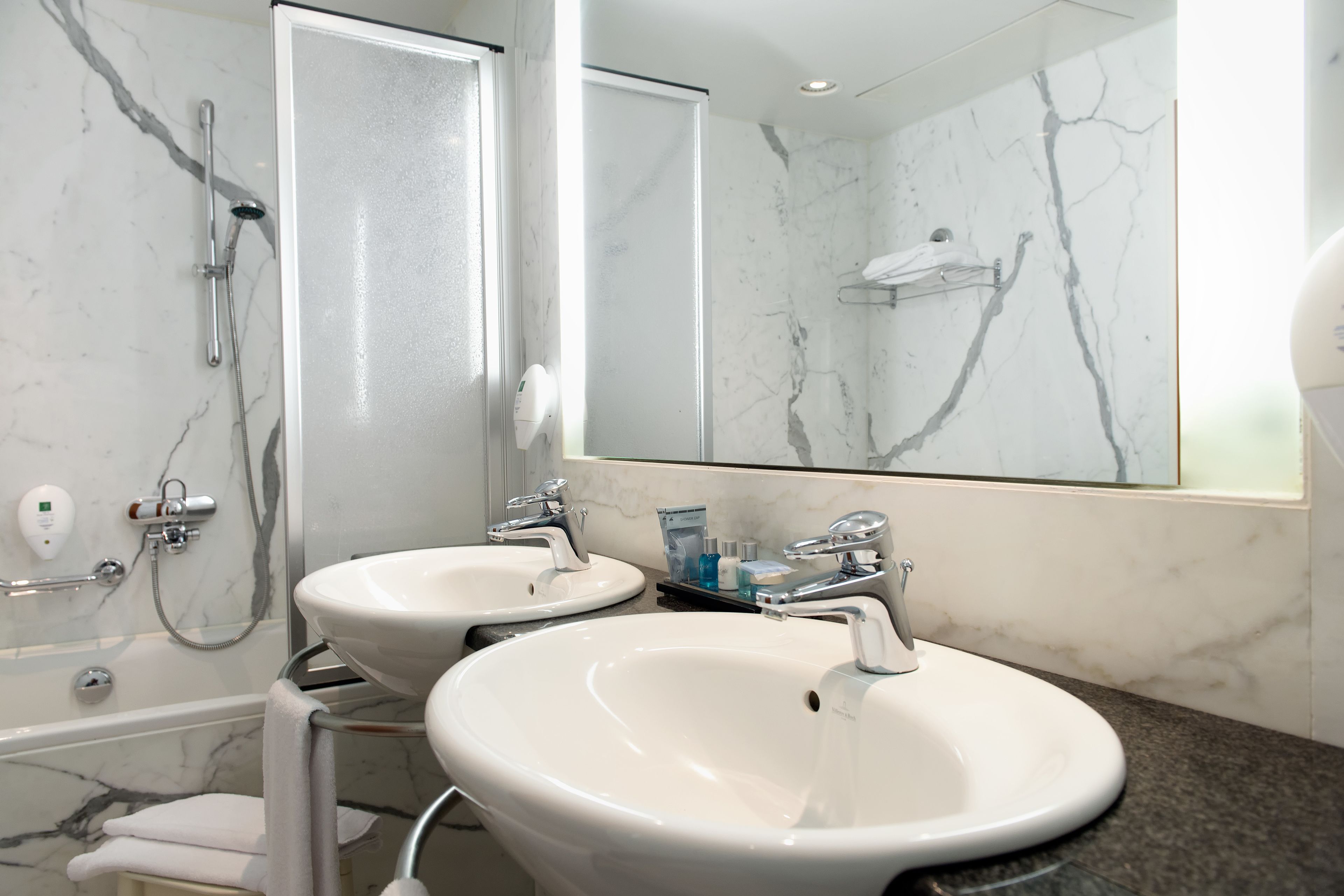 A bathroom with two sinks, a shower, and a large mirror.