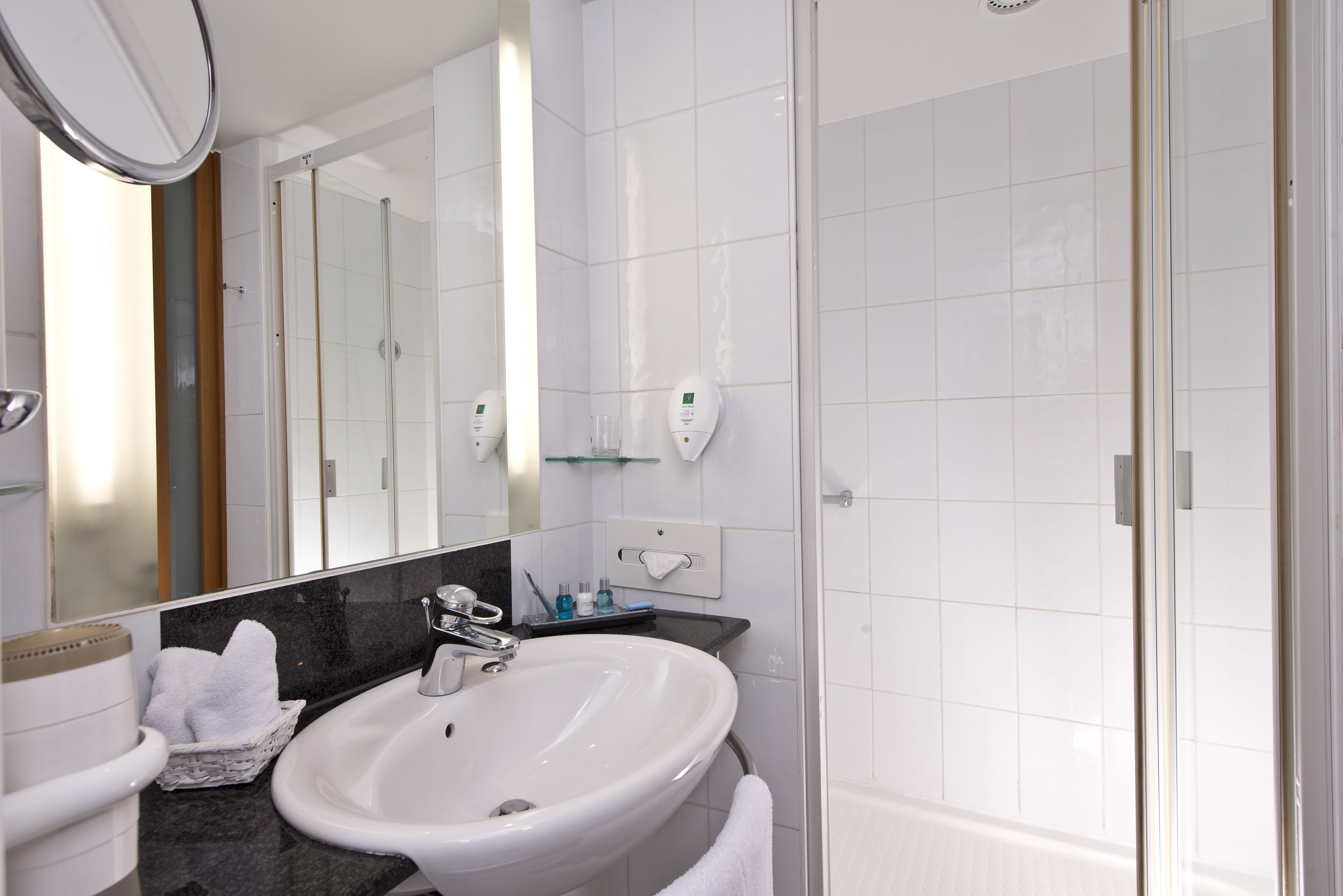 Un baño moderno con un lavabo blanco, un espejo grande y una cabina de ducha con puertas de cristal.