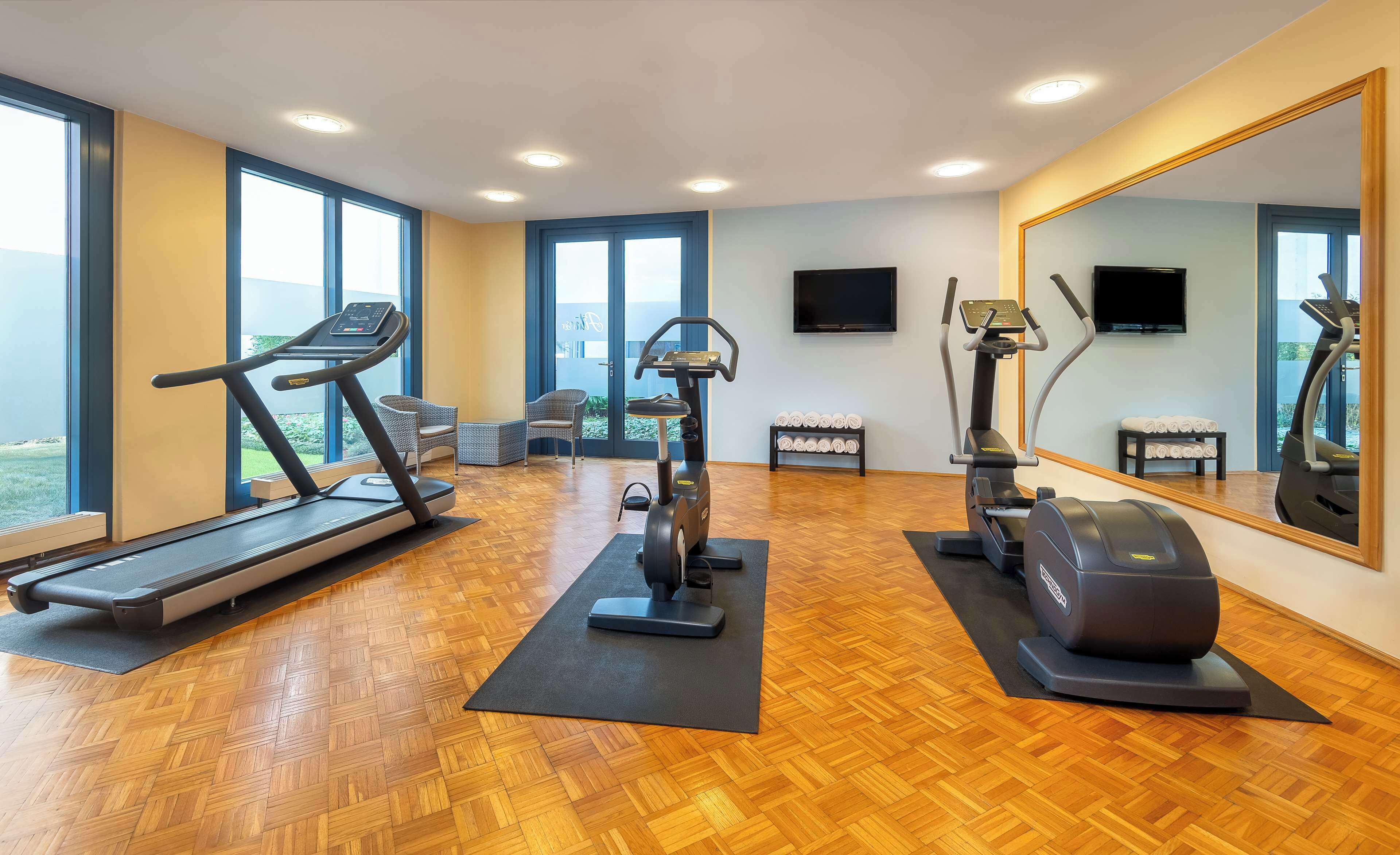 Ein Fitnessstudio mit Trainingsgeräten, großen Fenstern und einem Spiegel.