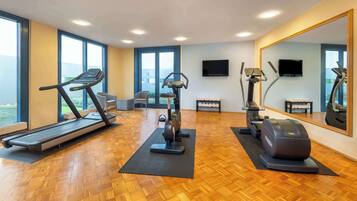 Ein Fitnessstudio mit Trainingsgeräten, großen Fenstern und einem Spiegel.