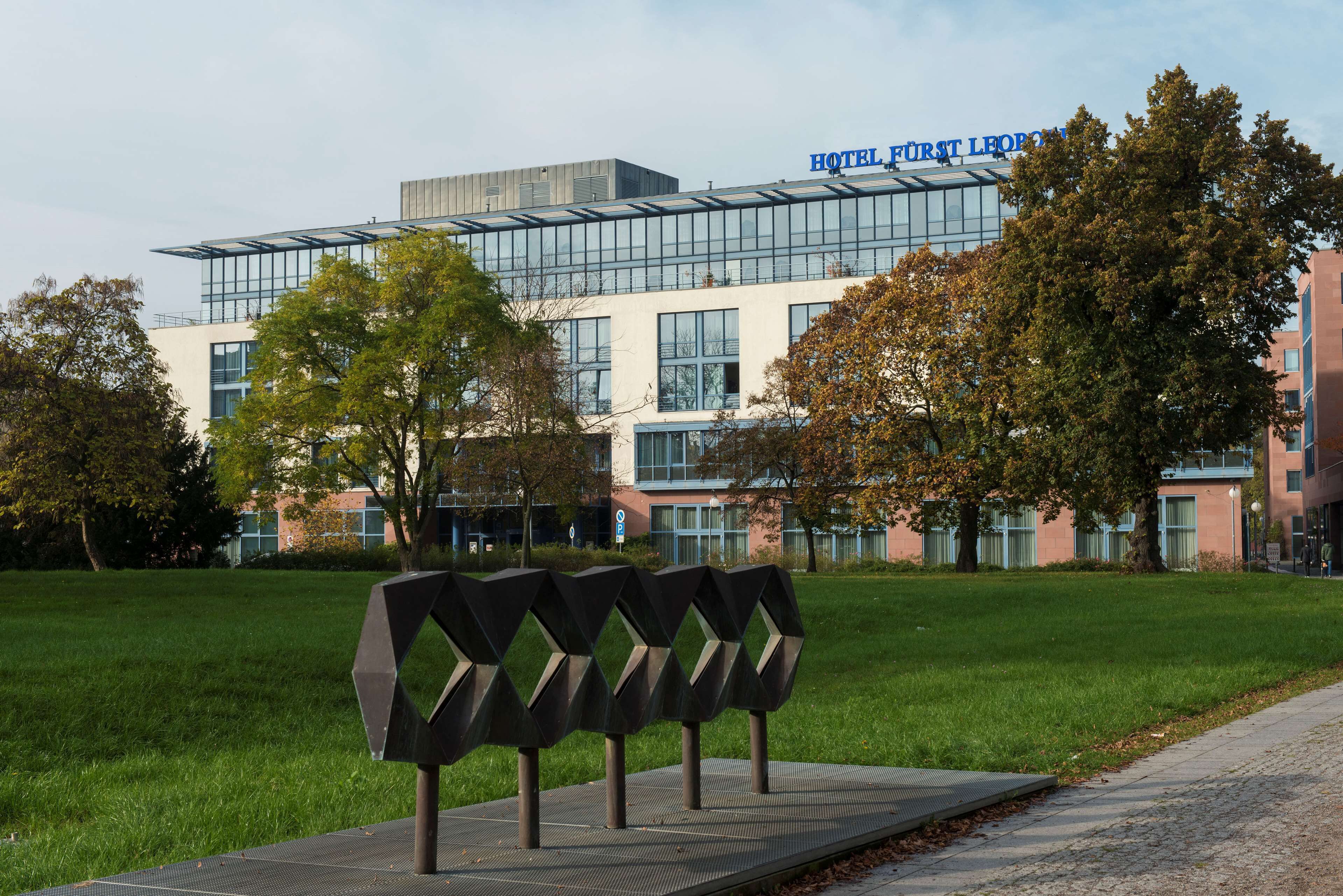 Een modern hotelgebouw met een glazen gevel en de naam 'HOTEL FÜRST LEIPZIG' is duidelijk zichtbaar.
