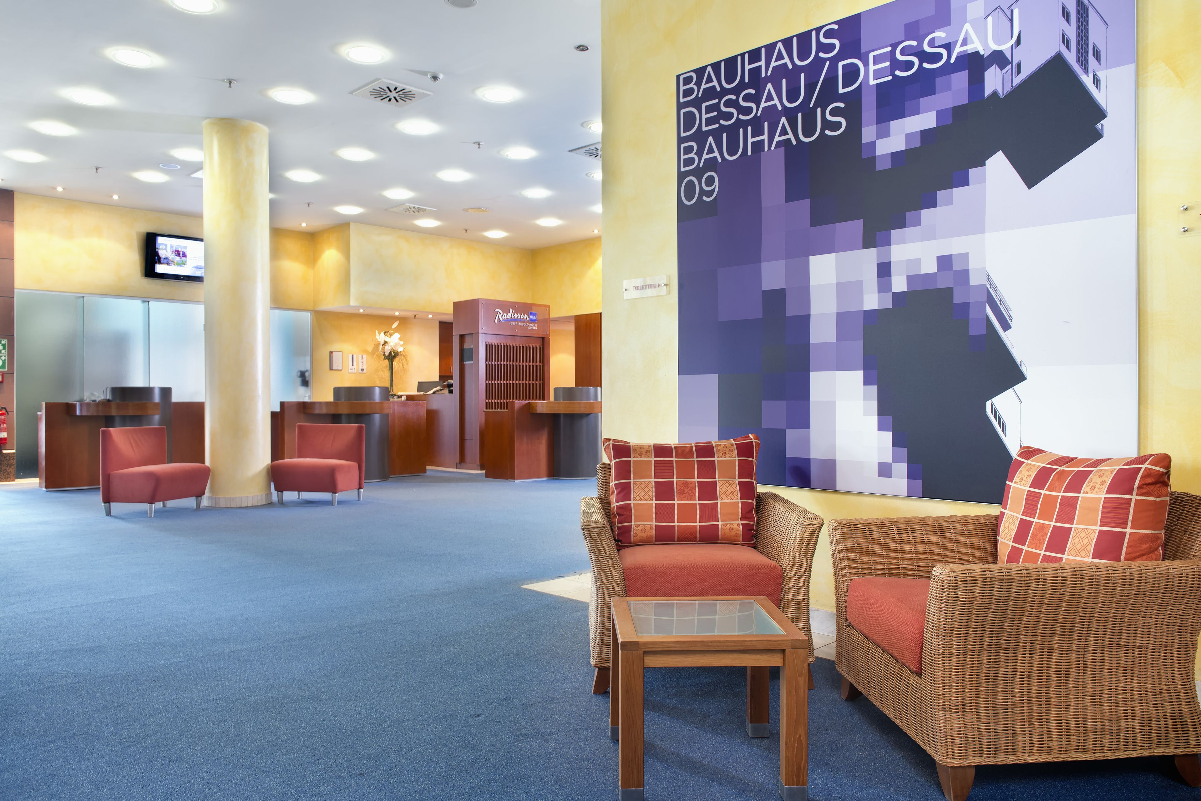 Eine Lobby mit Korbmöbeln, einem Empfangstresen und einem großen, pixeligen Poster an der Wand.