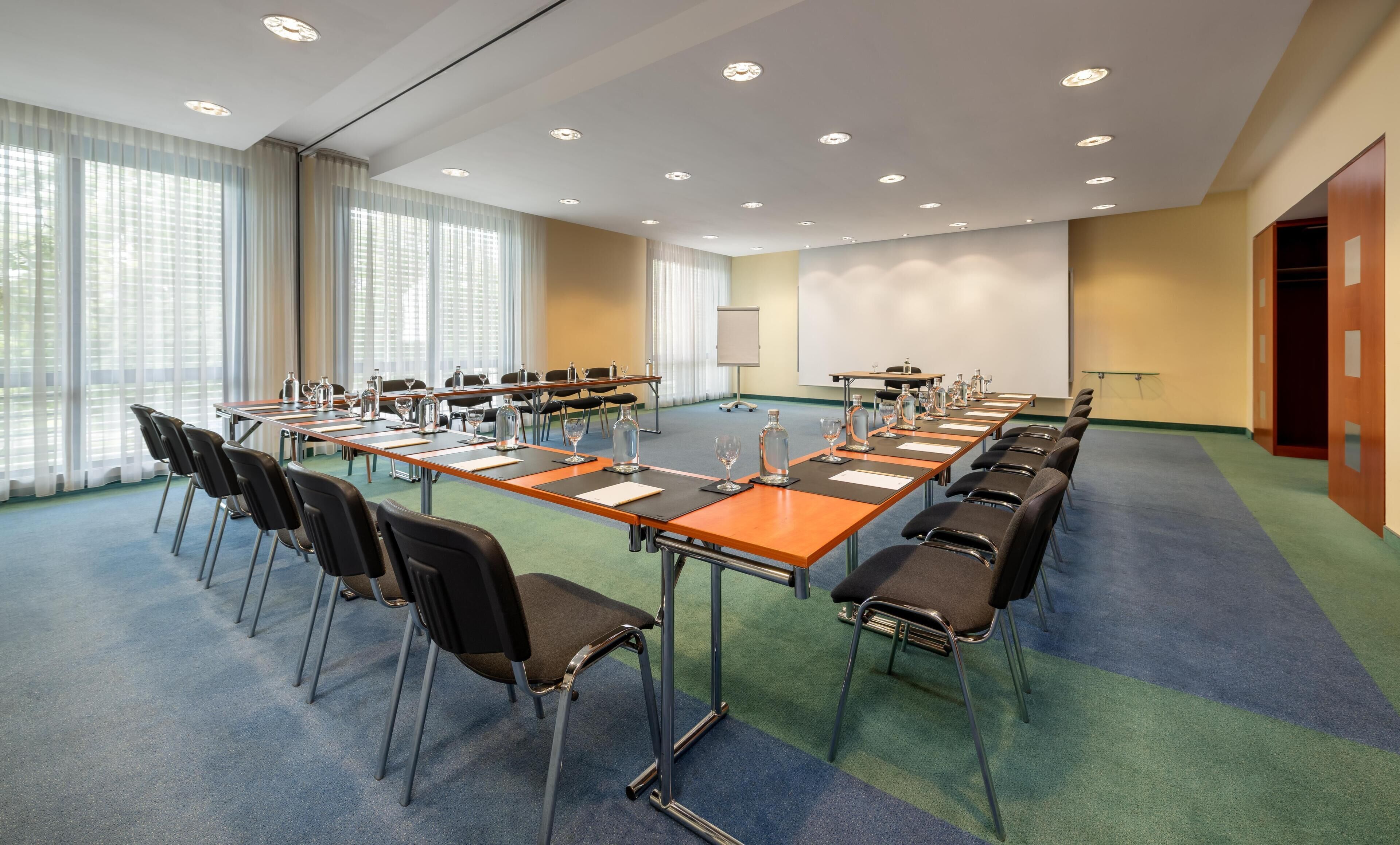 Un salón de conferencias con una larga mesa, sillas y una pantalla para proyector.