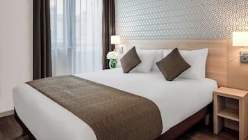 Une chambre d’hôtel avec un grand lit, une tête de lit en bois, une table de chevet, une lampe et un mur orné d’un motif.
