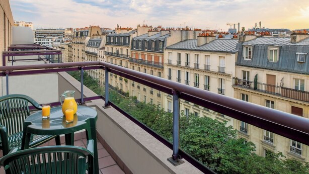 Un balcon avec une table, des chaises et une carafe de jus d’orange.