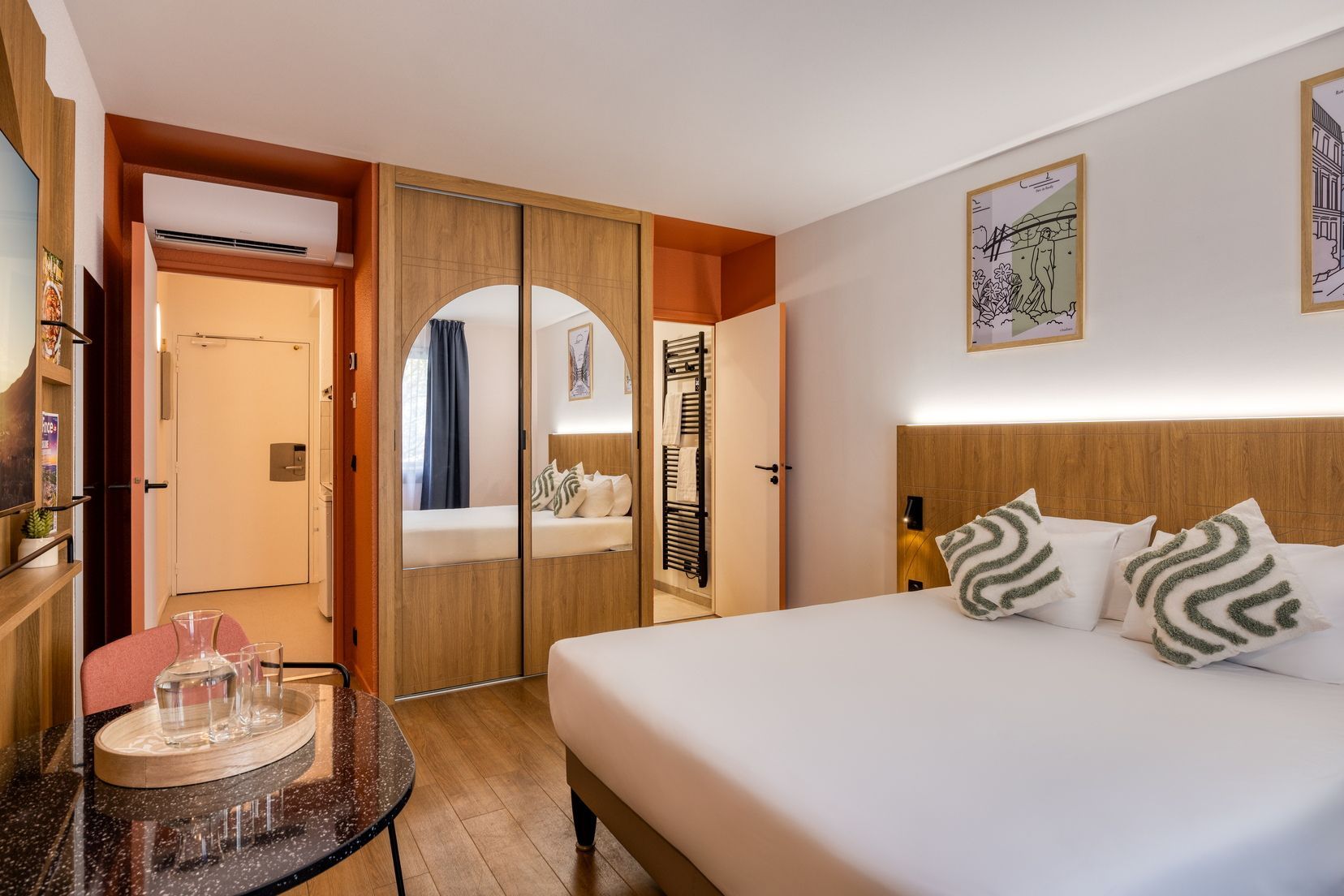 Una habitación de hotel con una cama, un escritorio con bandeja, un espejo y un armario.