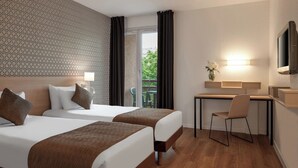 Une chambre d’hôtel avec deux lits, un bureau, une chaise, une télévision et un balcon donnant sur un espace verdoyant.