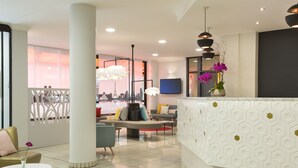 Un hall d’hôtel moderne doté d’un comptoir d’accueil, d’un espace salon et de grandes fenêtres offrant une vue sur le paysage urbain.