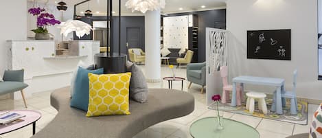 A modern living room with a curved sofa, a glass coffee table, and a small round table with a vase. There are chairs, a bookshelf, and a wall-mounted artwork.