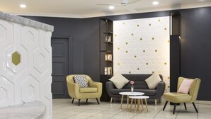 Een moderne woonkamer met twee fauteuils, een bank en een kleine salontafel. Er is een boekenkast en een decoratief wandpaneel.