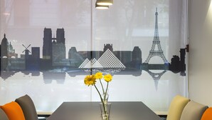 Une table ornée d’un vase de fleurs jaunes, avec une vue sur la ville et des sièges aux couleurs orange et grise.