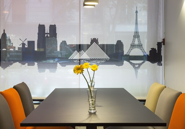 Une table ornée d’un vase de fleurs jaunes, avec une vue sur la ville et des sièges aux couleurs orange et grise.