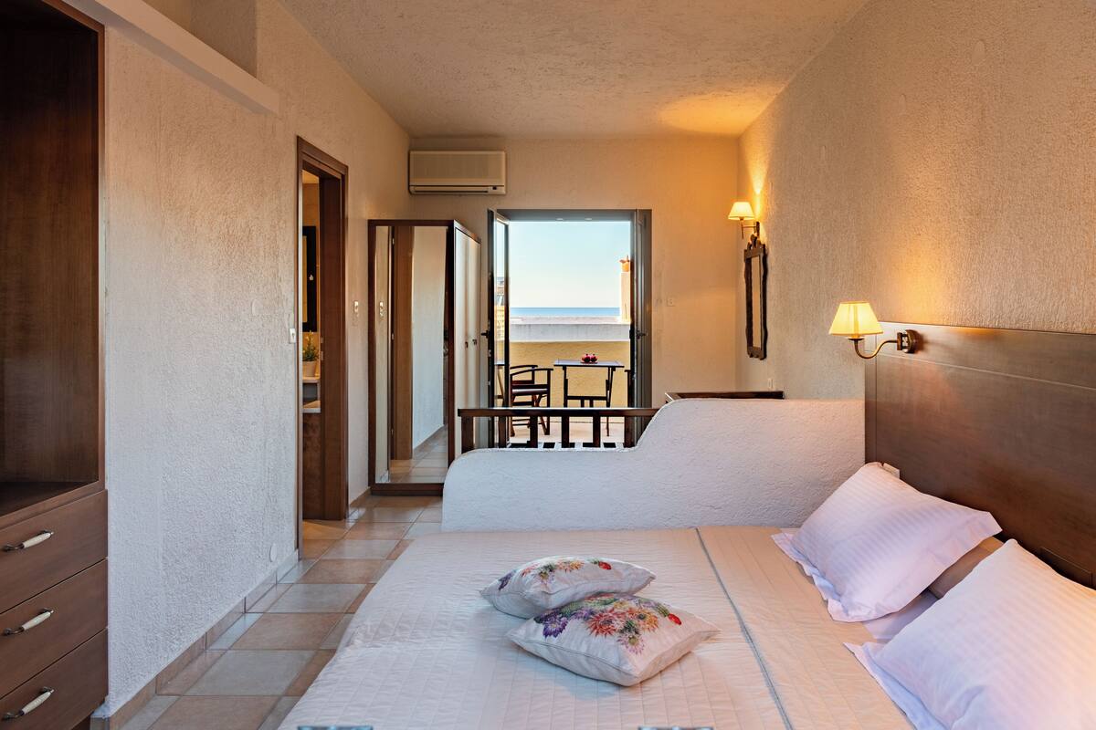 Een hotelkamer met een bed, nachtlampjes, een kledingkast en uitzicht op het strand.