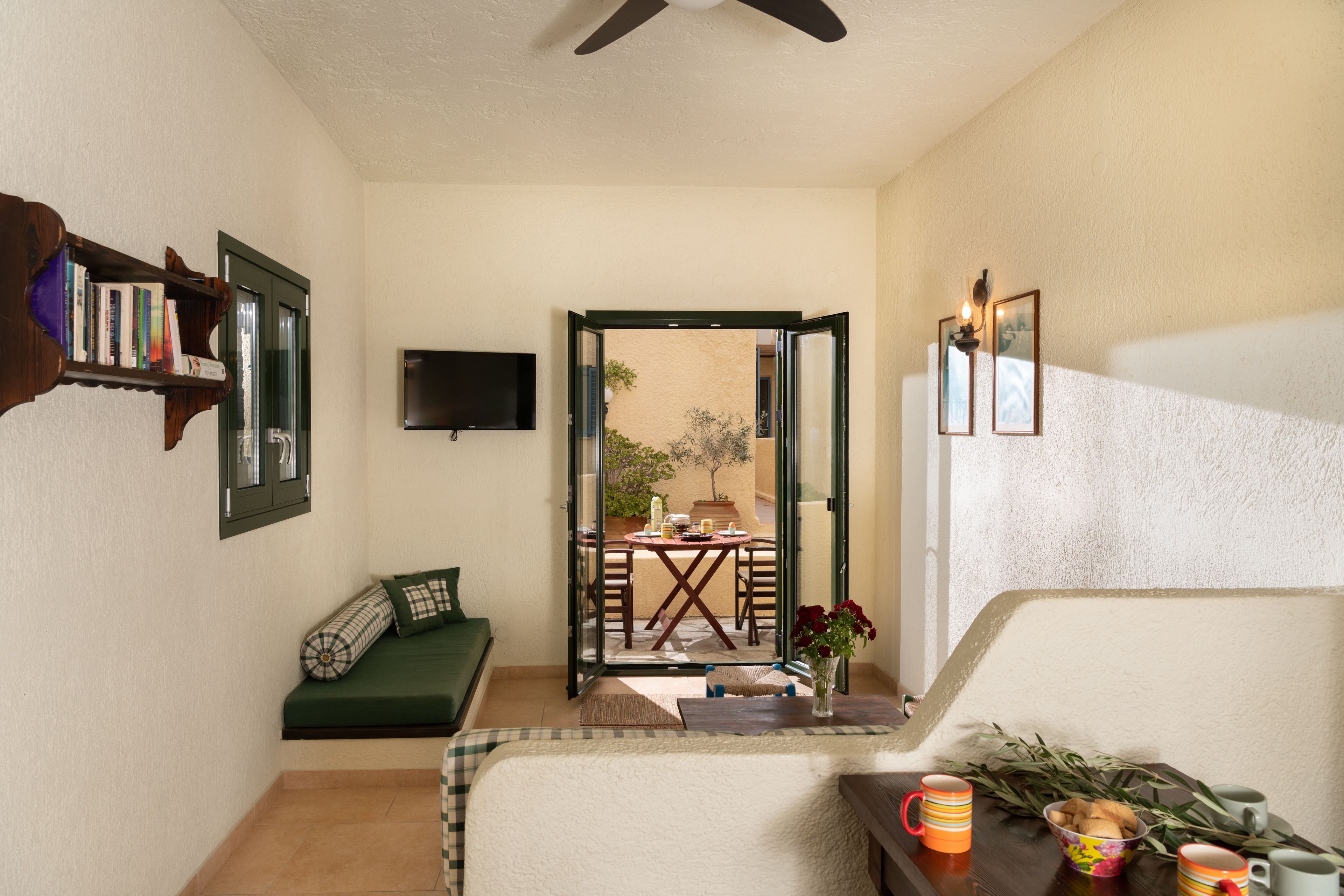 Une chambre d’hôtel avec un canapé vert, une table à manger avec des chaises, un téléviseur fixé au mur et un balcon avec une table et des chaises.