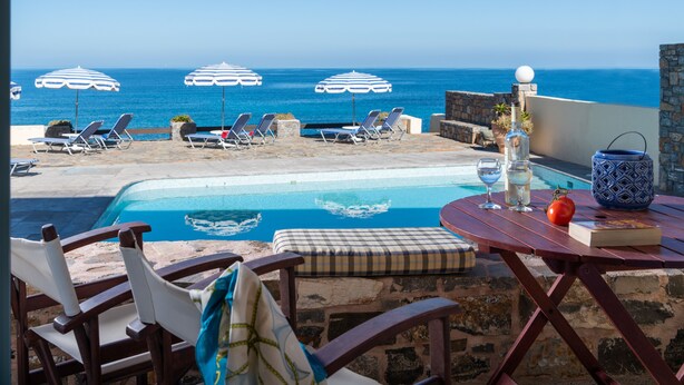 Zona junto a la piscina con sillones de descanso y sombrillas, una mesa con una botella, vasos y un libro, y vista al océano.
