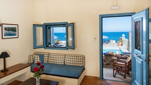 Una habitación con vista al mar, un sofá con cojines escoceses, una mesita con un florero y una puerta que da al exterior.