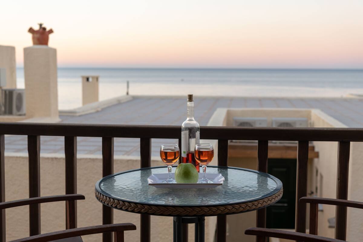 Een tafel met een fles en glazen op een balkon met uitzicht op een strand.