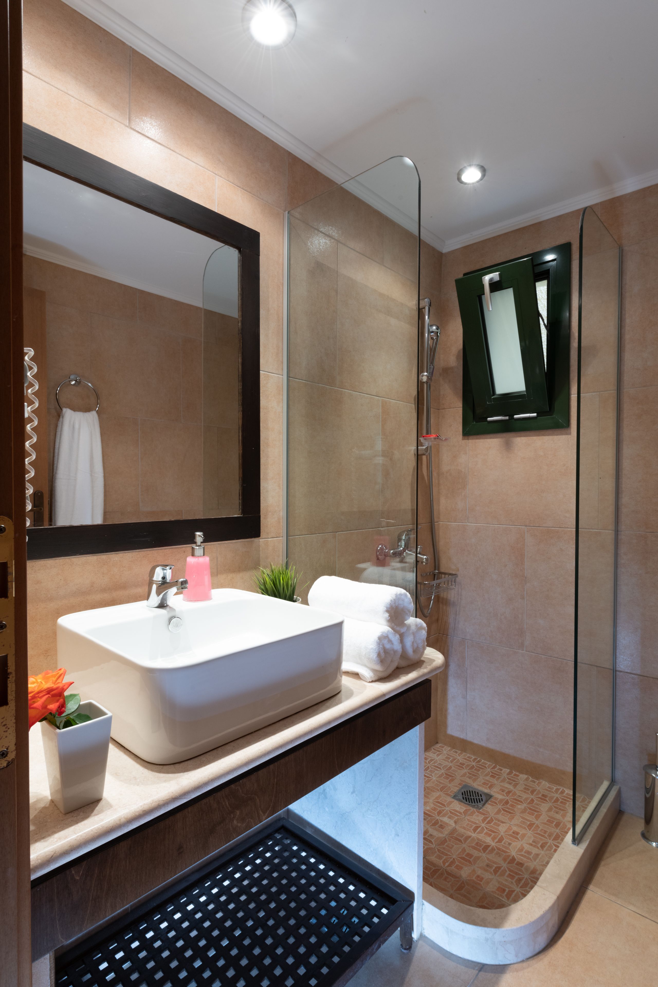A modern bathroom with a large mirror, a sink, a shower, and a small plant.