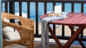 Una terraza de madera con una silla de mimbre y una mesa, con vista a una playa.