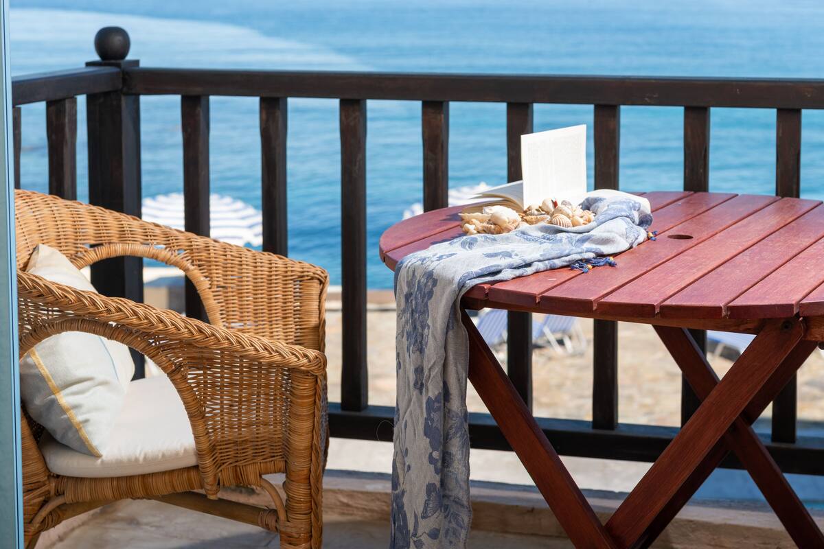Een houten terras met een rieten stoel en een tafel, met uitzicht op een strand.