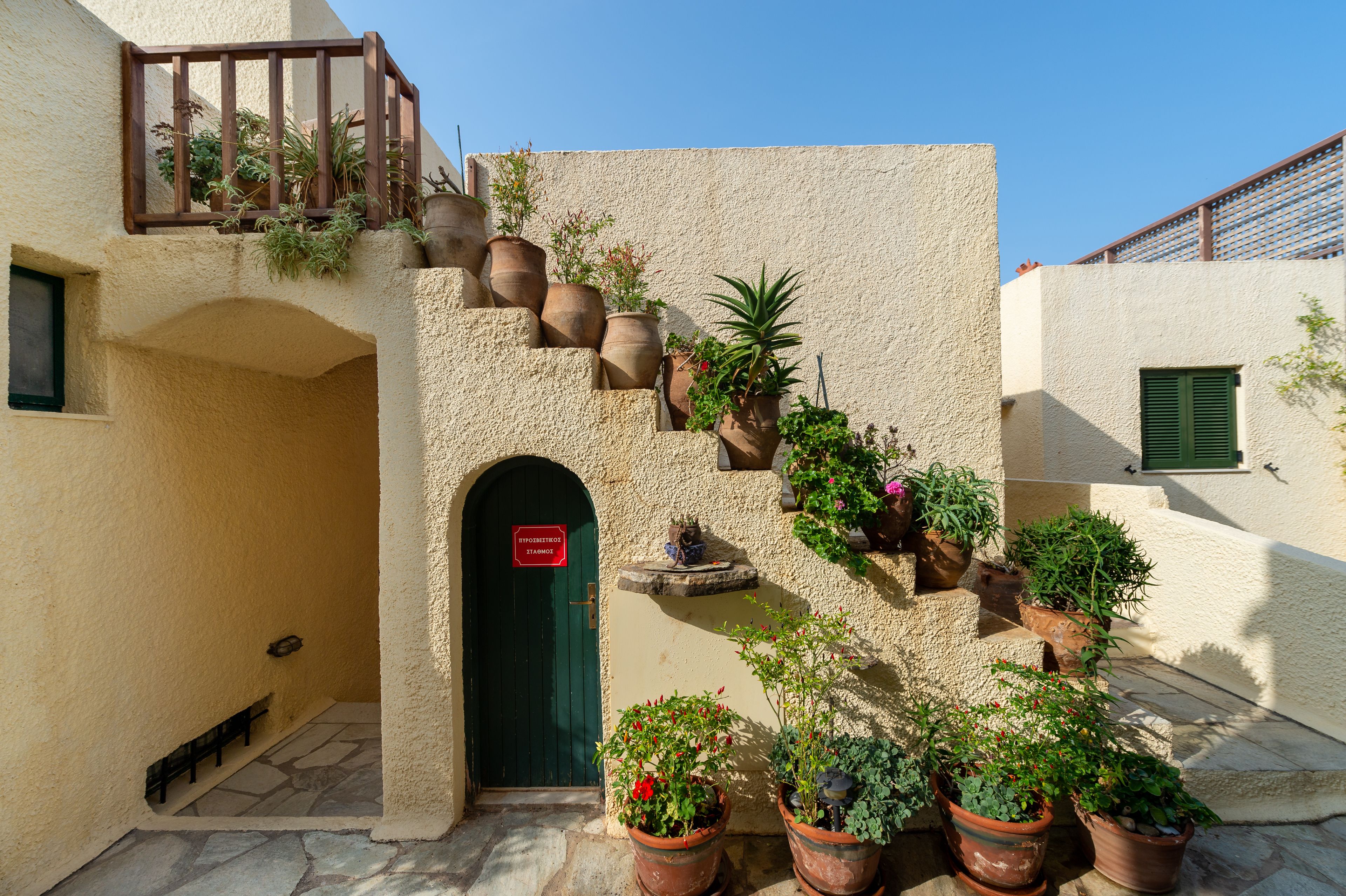 A courtyard with a staircase surrounded by potted plants, a green door, and a small fountain.