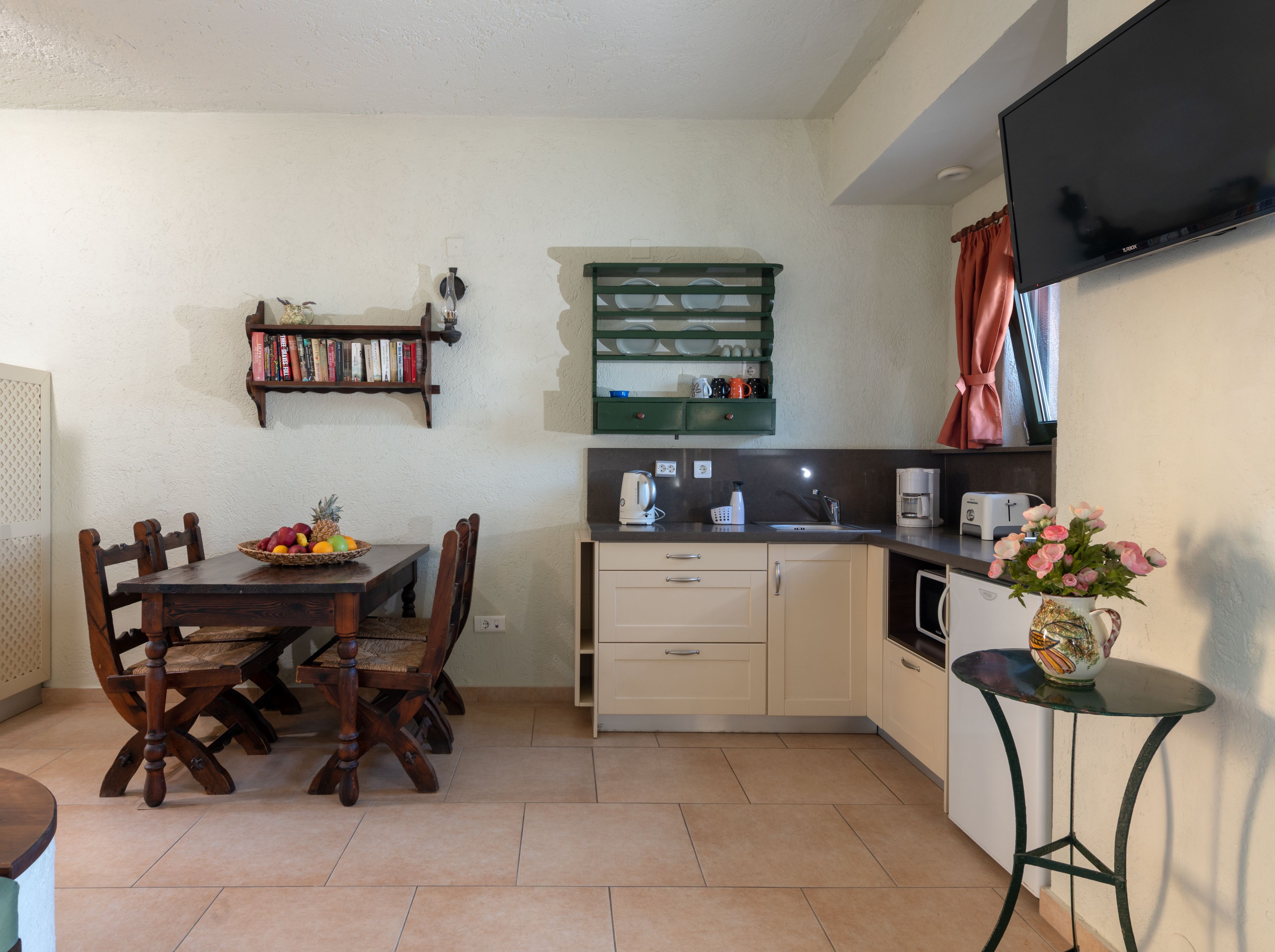 Una cocina compacta con una mesa de comedor, sillas, una cafetera y un televisor de pantalla plana montado en la pared.