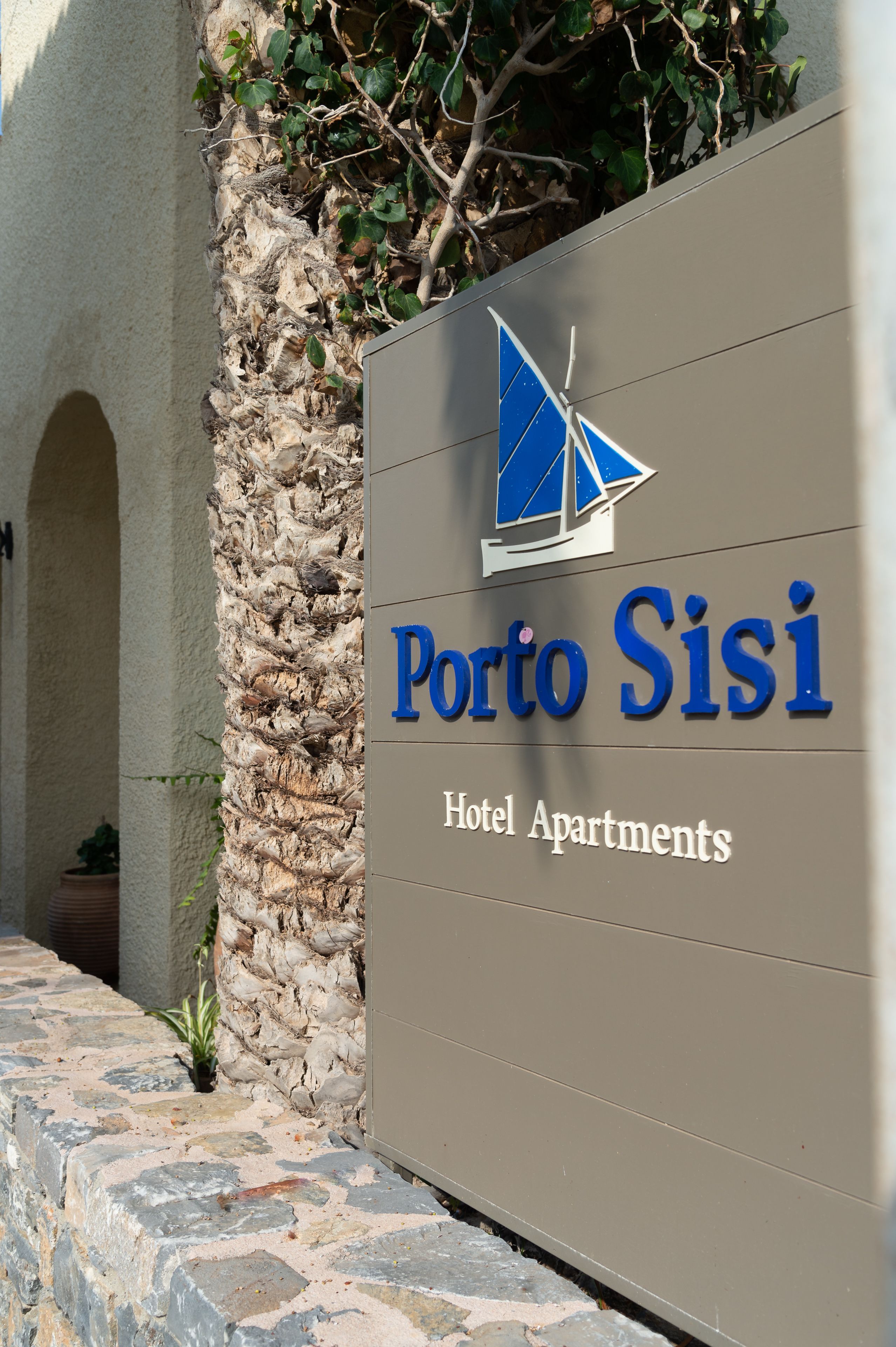A sign for Porto Sisi Hotel Apartments with a sailboat logo.