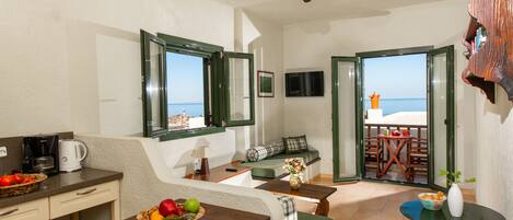 A room with a kitchenette, seating area, and a view of the sea.