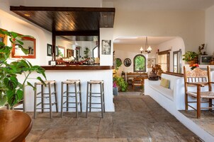 Amplia sala de estar con barra, taburetes de madera, sofá y mesa de comedor.