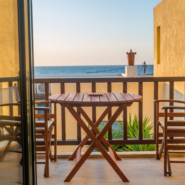 Une table en bois et deux chaises sur un balcon donnant sur la mer, avec une tour de surveillance des sauveteurs en vue.