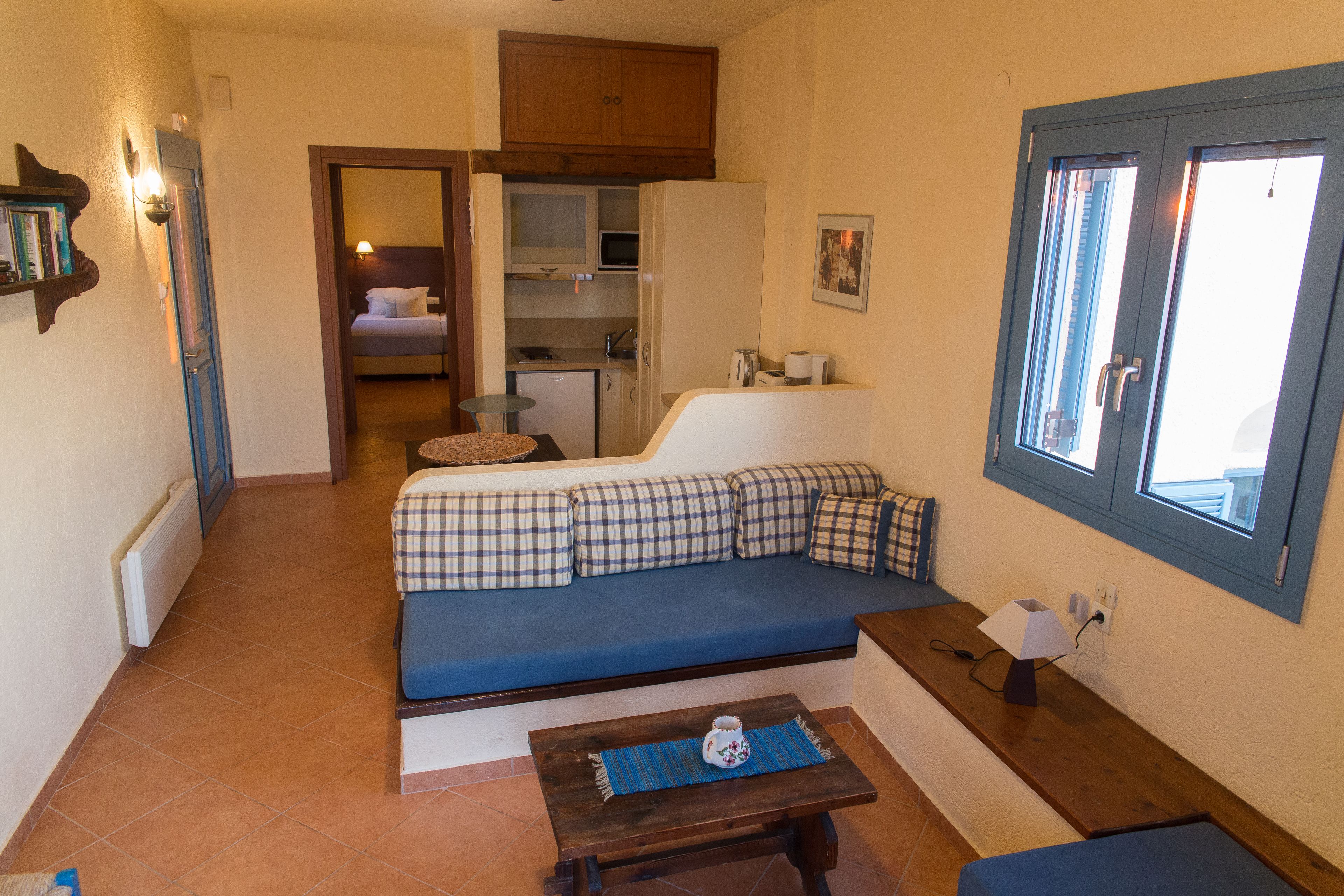 Een knus woongedeelte met een blauwe bank, een kitchenette en een eettafel.