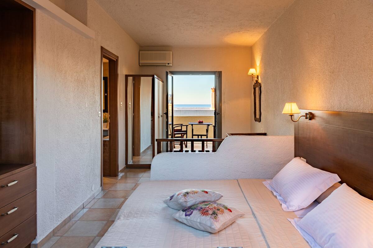 Een hotelkamer met een bed, nachtlampjes, een kledingkast en uitzicht op het strand.