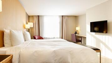 A hotel room with a large bed, a desk, a chair, a TV, and a bathroom visible through a door.