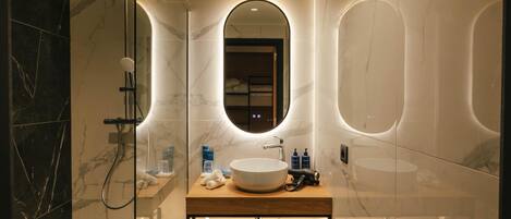 Un baño moderno con un espejo grande, un lavamanos y una zona de ducha.