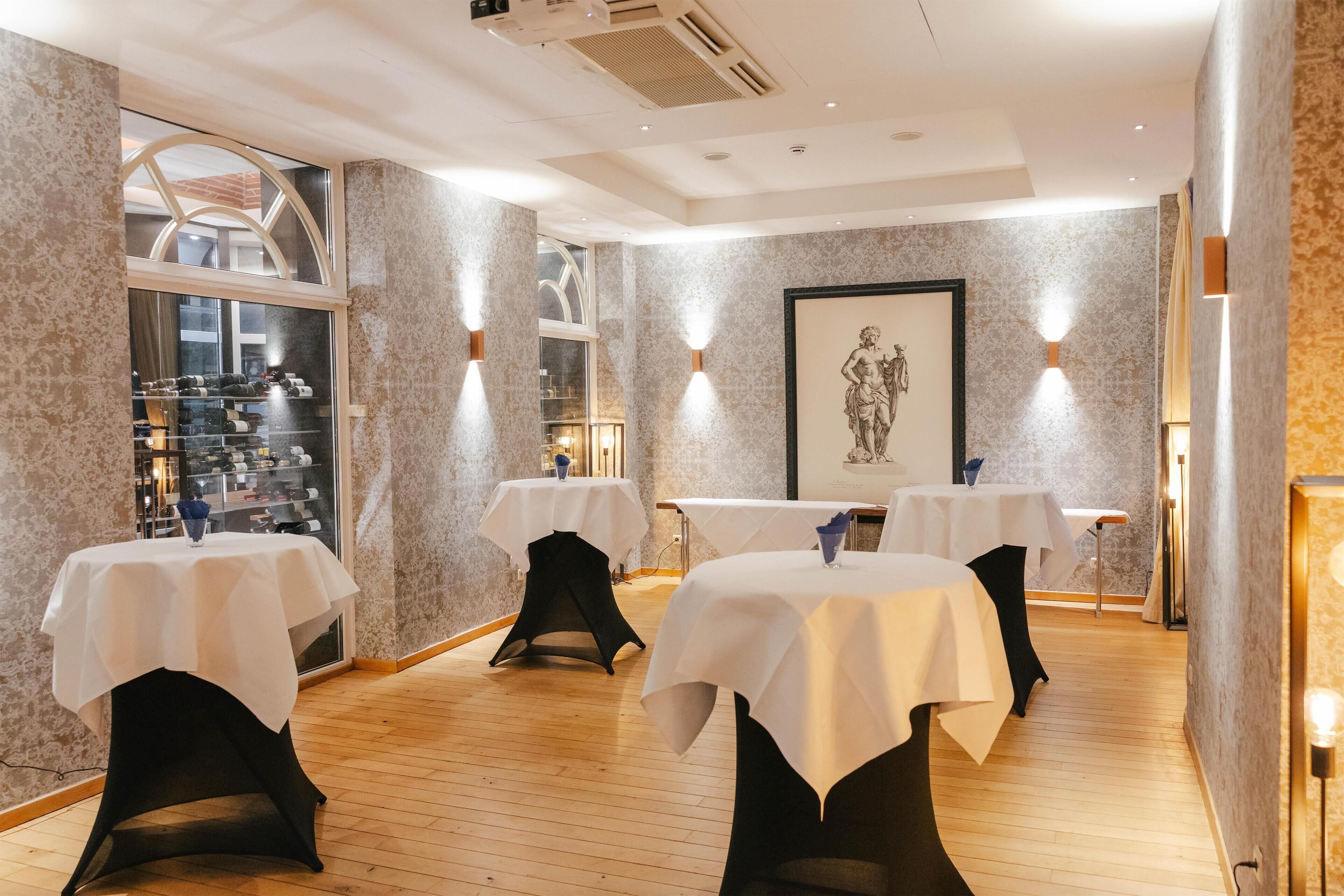 A restaurant with tables covered in white tablecloths, wooden flooring, and wall-mounted lighting.