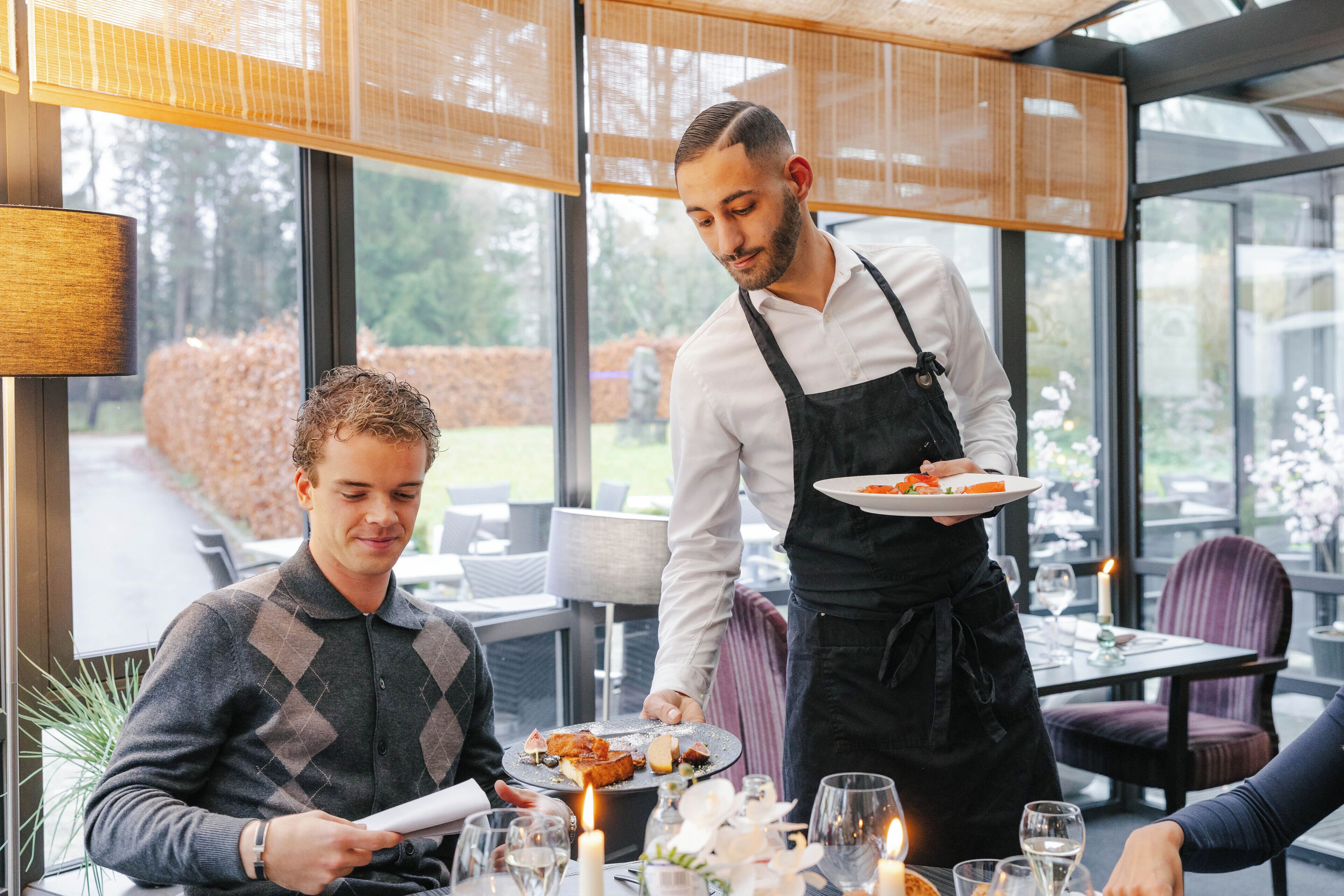 En restaurang där en servitör serverar en rätt till en gäst som sitter vid ett bord.