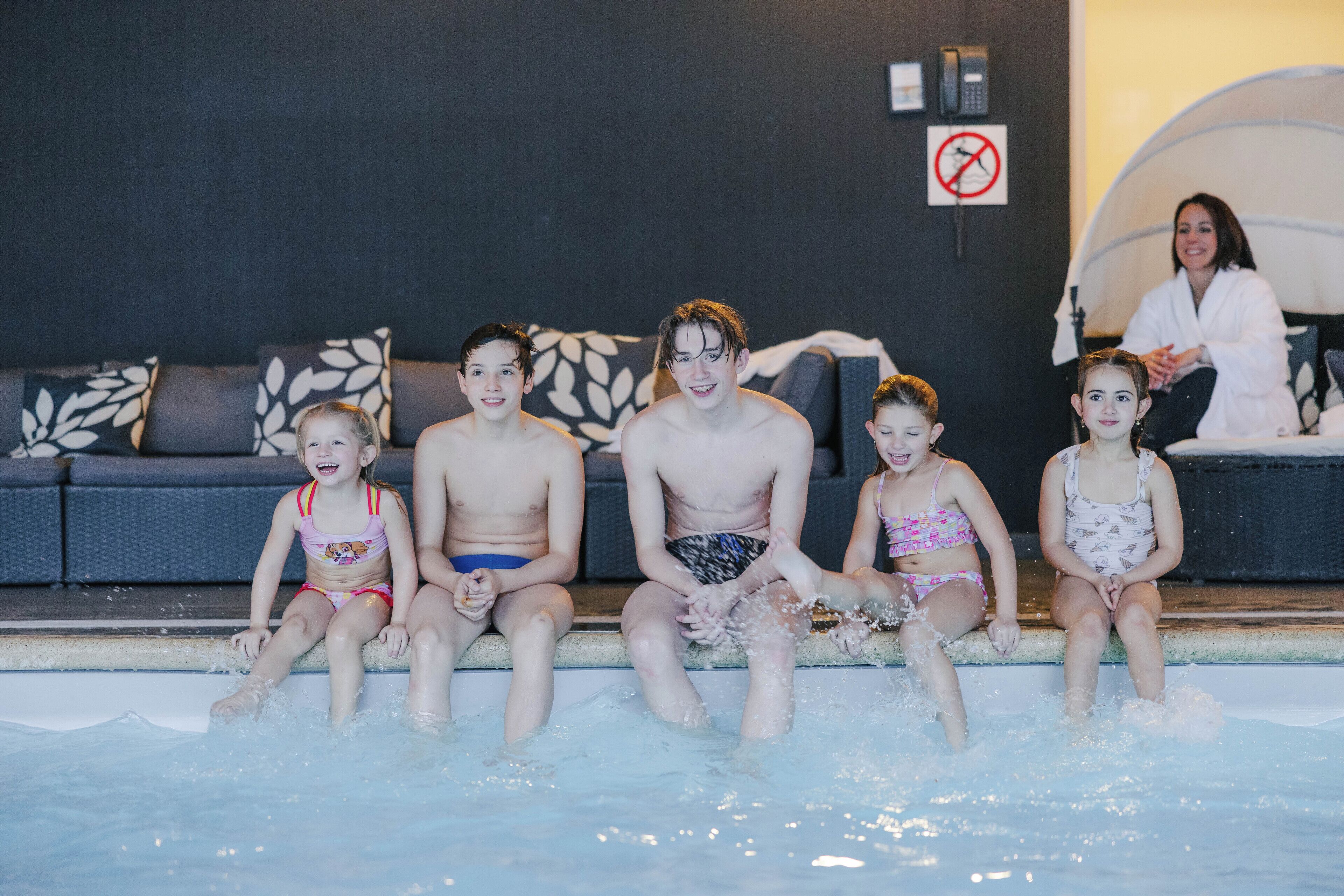 Una familia de cinco personas sentada junto a una piscina, con un sofá y un letrero de prohibido fumar al fondo.