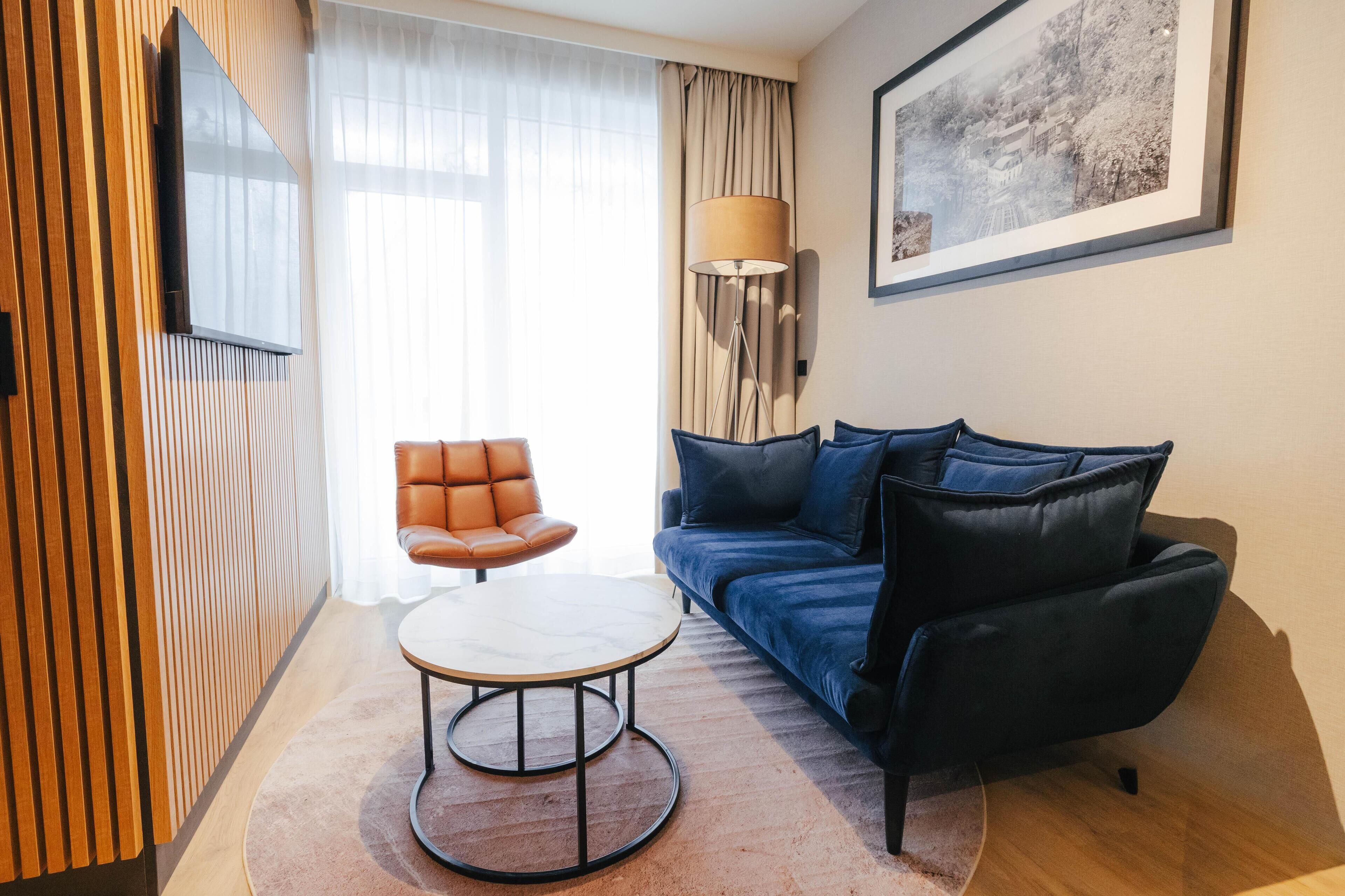 Un salon moderne comprenant un canapé, un fauteuil, une table basse, un téléviseur fixé au mur et une lampe.
