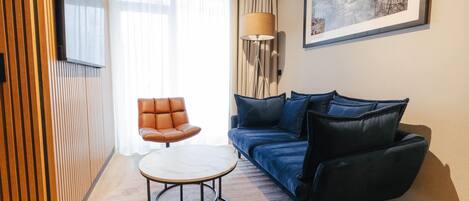 Un salon moderne comprenant un canapé, un fauteuil, une table basse, un téléviseur fixé au mur et une lampe.