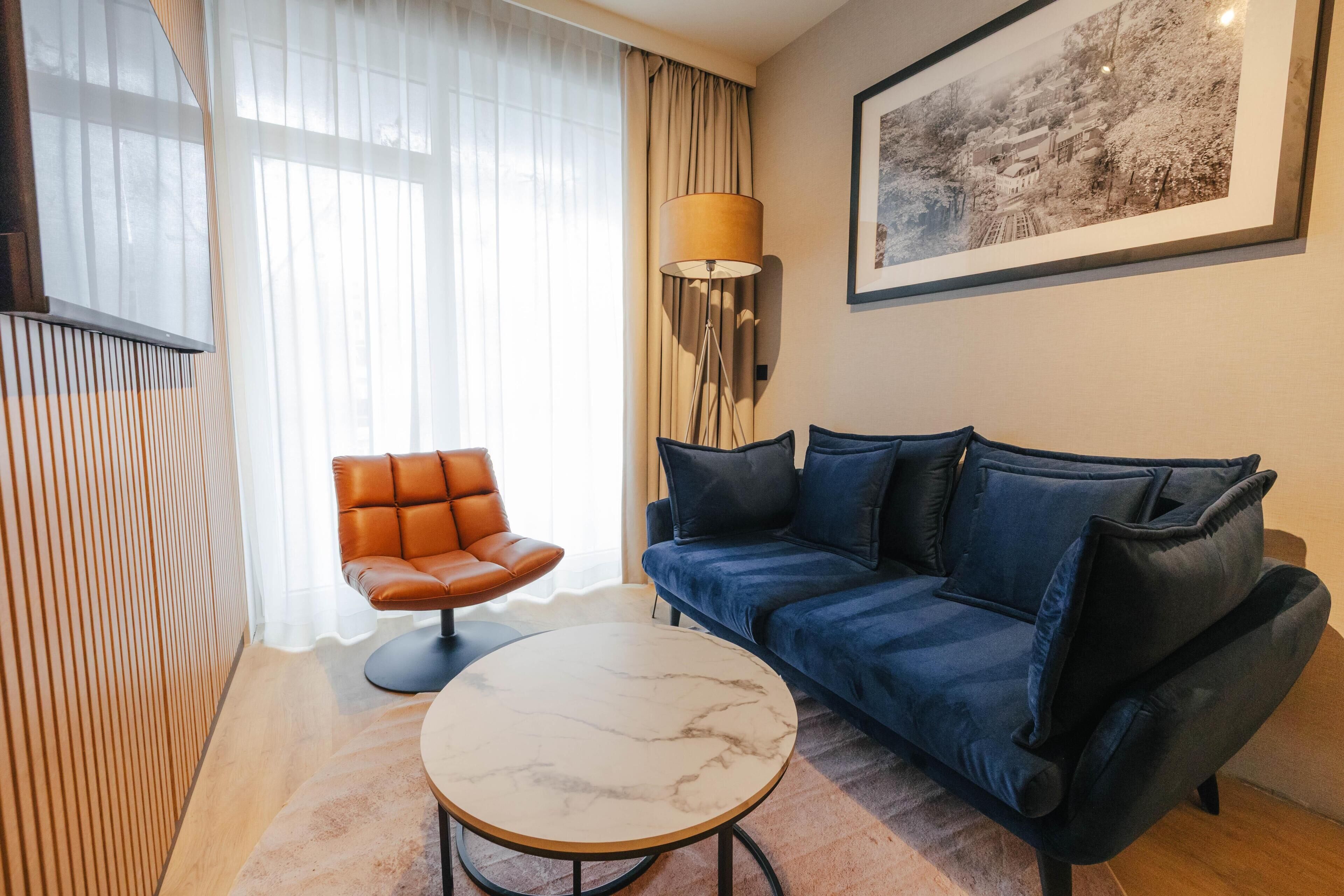 Un salon moderne avec un canapé, un fauteuil, une table, une lampe et un tableau encadré accroché au mur.