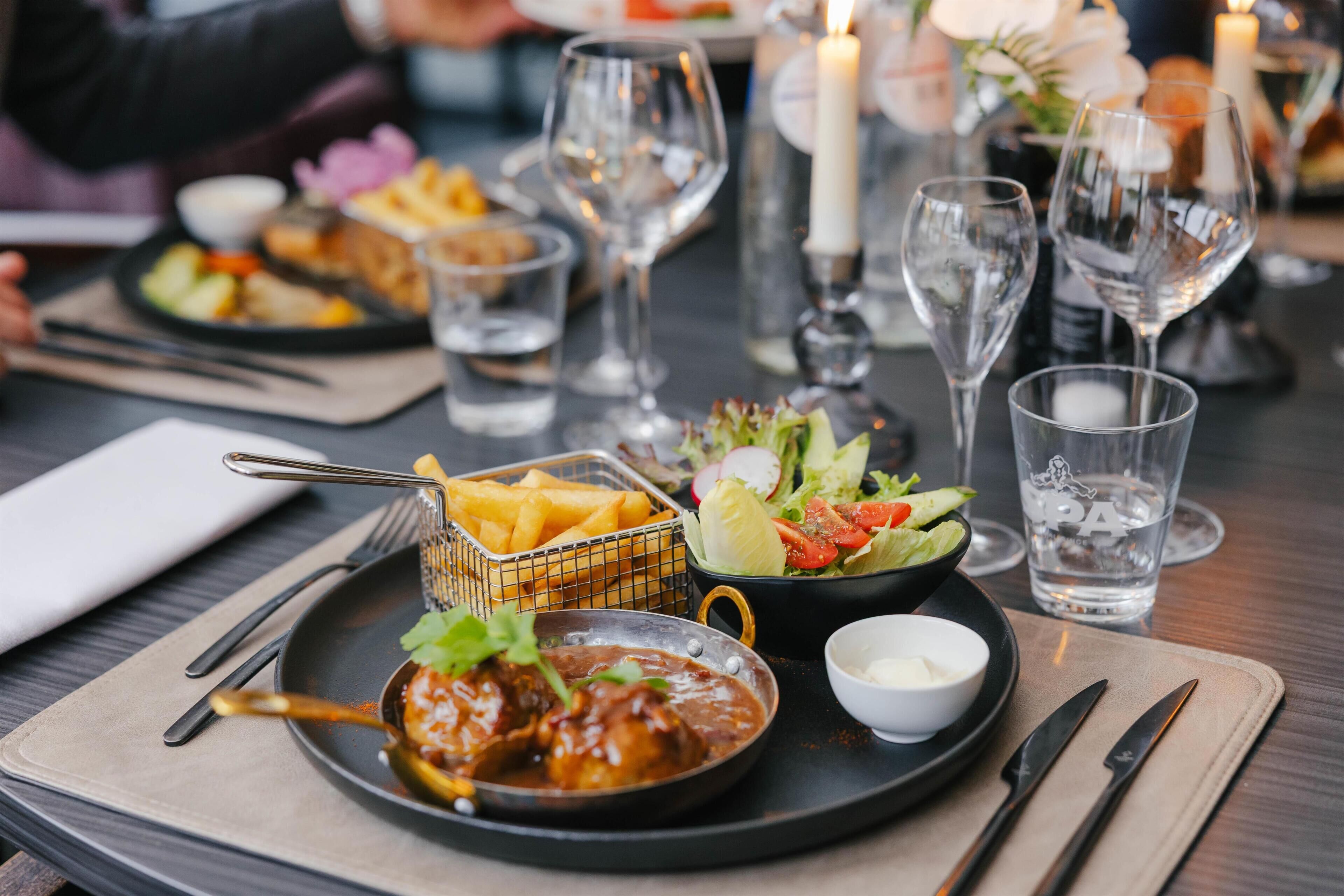 A dining table set with a plate of food, a small bowl of sauce, a glass of water, and a candle.