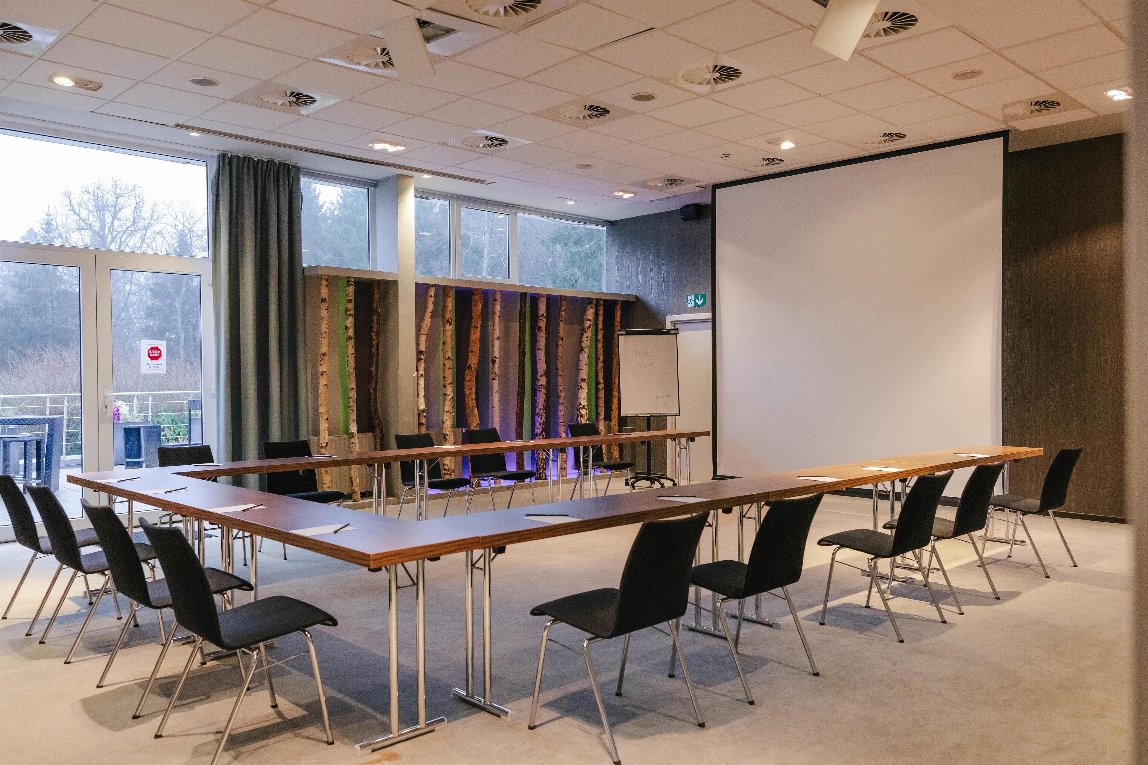 A conference room with a long table, black chairs, a whiteboard, and a projector screen.