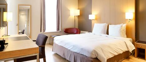 Una habitación de hotel con cama, mesitas de noche, escritorio, silla y espejo.
