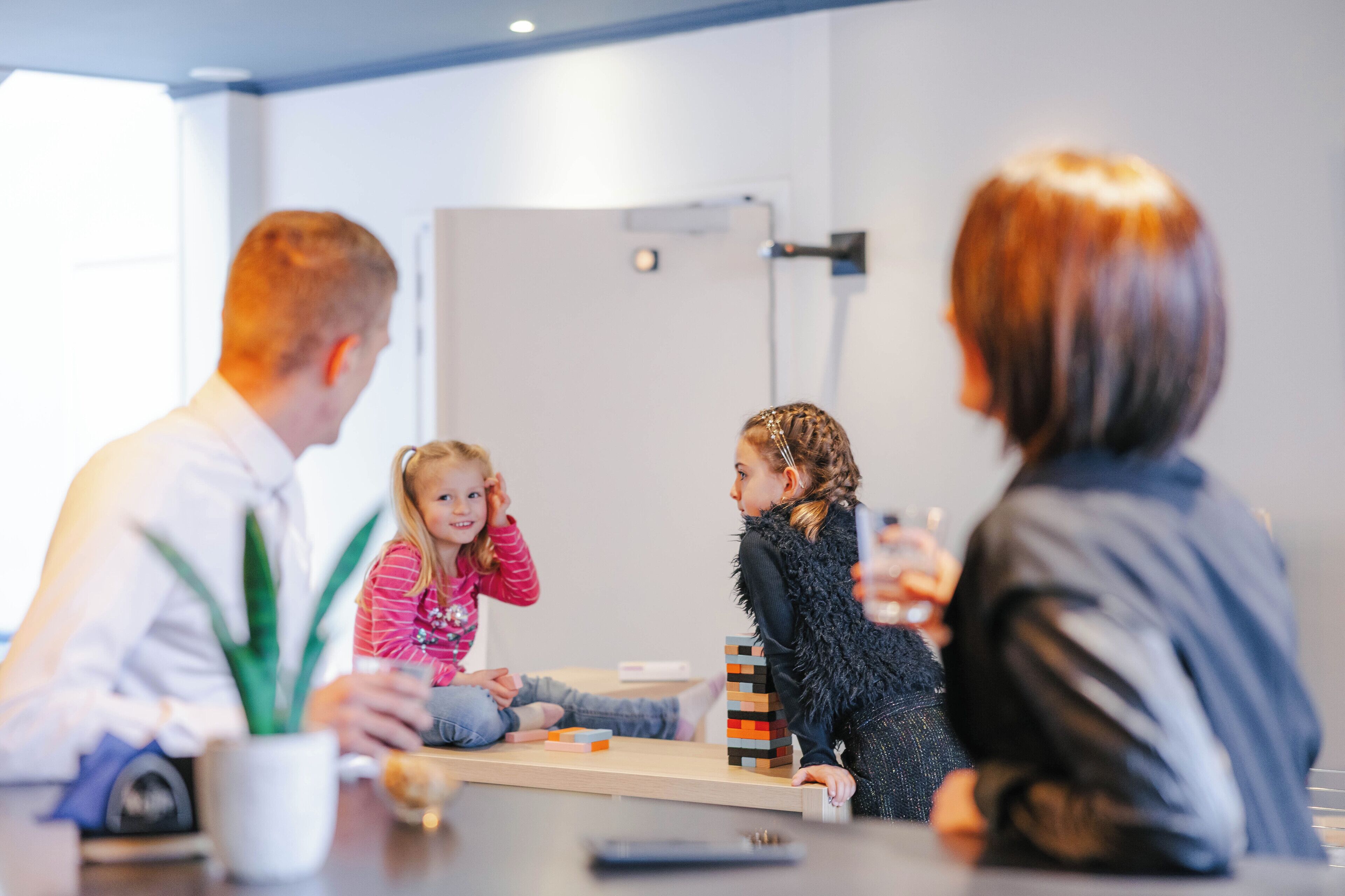 A group of people sitting around a table with a whiteboard and a plant in the room.